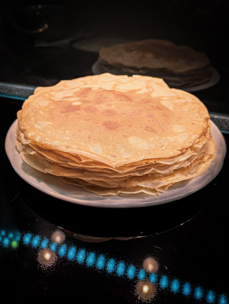 Delicious stack of thin crepes neatly arranged on a white plate, ready to serve.