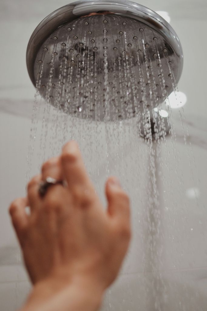 A hand reaches toward a shower head, capturing water droplets in motion.