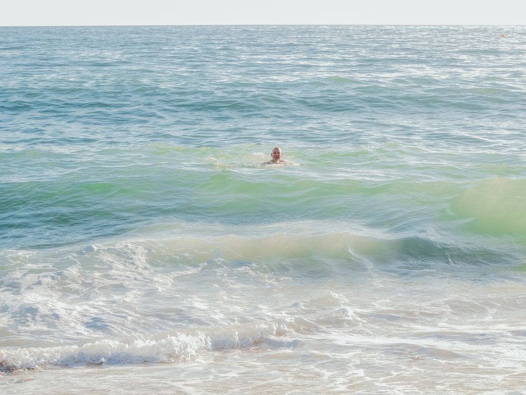 A solitary adult swims in the tranquil waves, enjoying the sea's calm embrace on a sunny day.