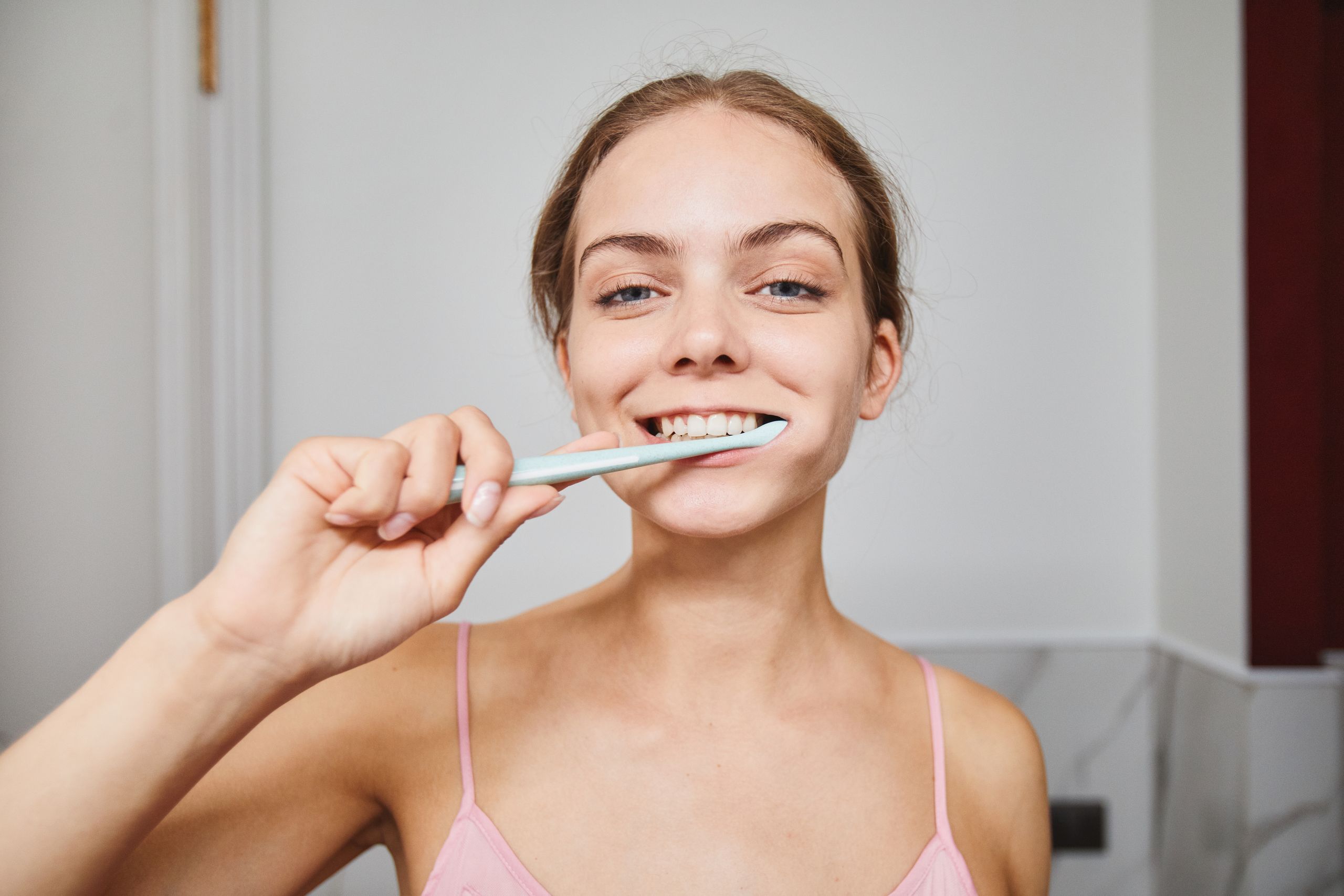 Close-up of a woman smiling while brushing teeth in a modern bathroom.