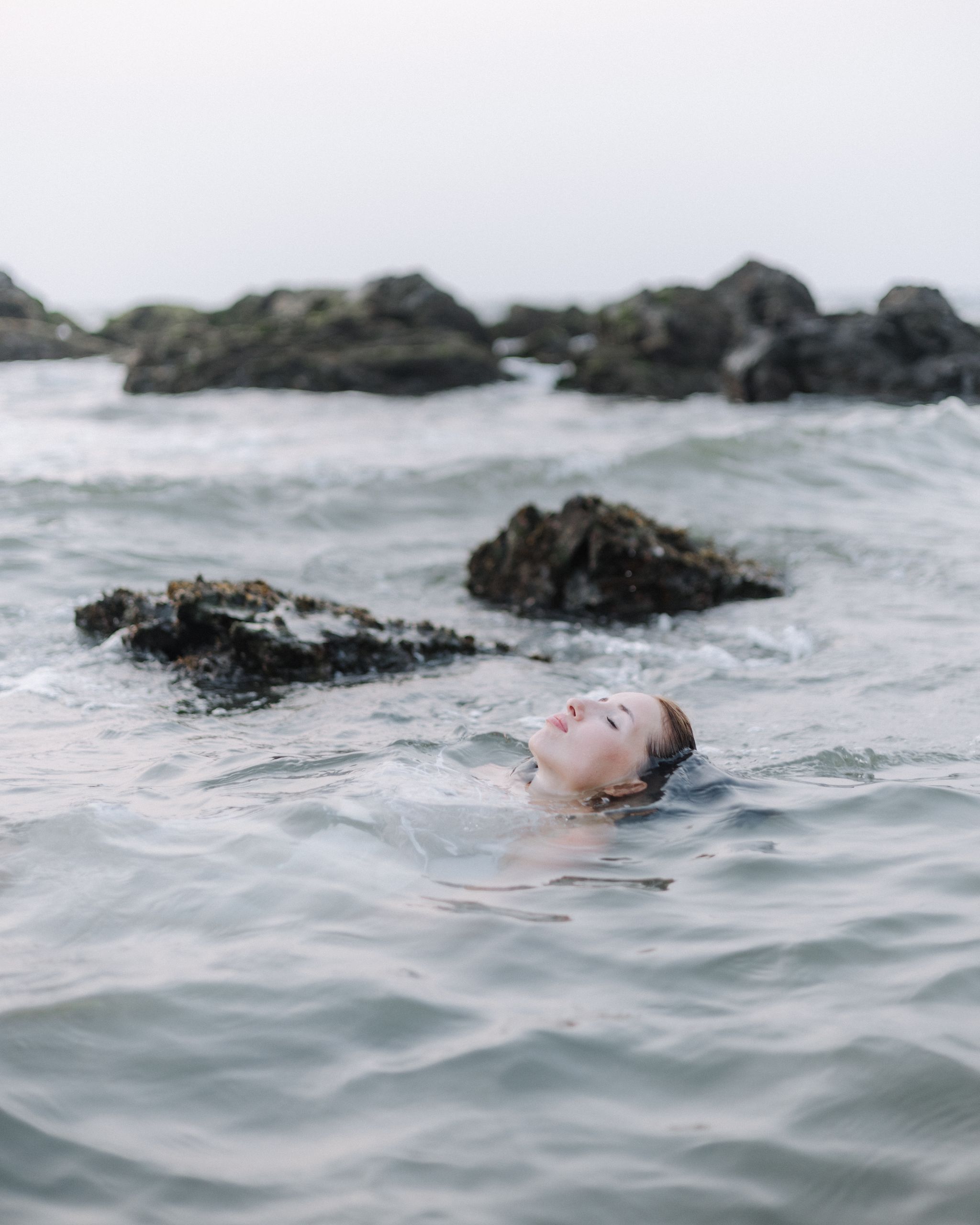 Peaceful scene of a woman floating in the ocean with rocky background, eyes closed.